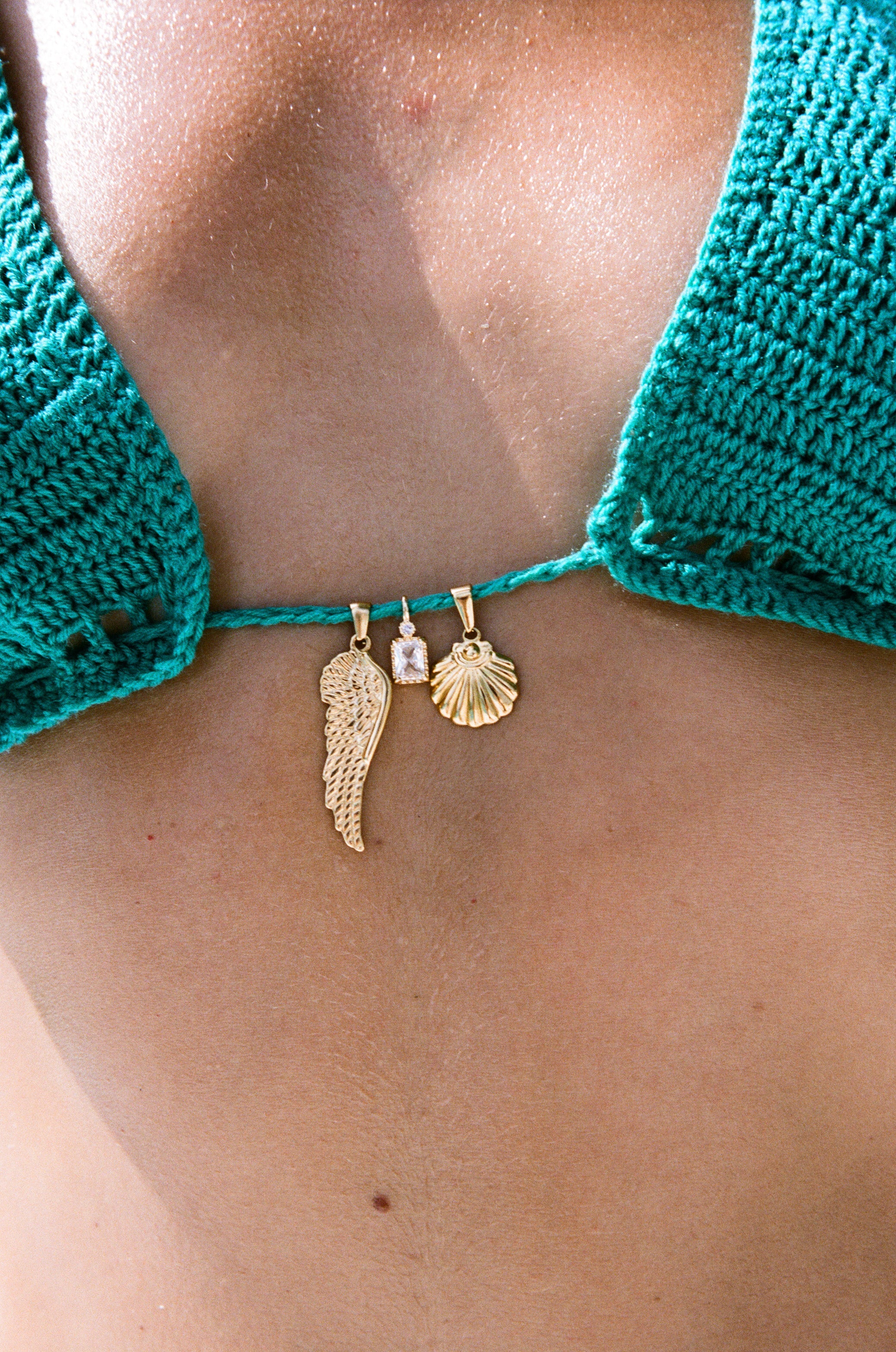 Close up of model wearing an emerald, adjustable-cup, crochet bikini top featuring 18k gold charm details.
