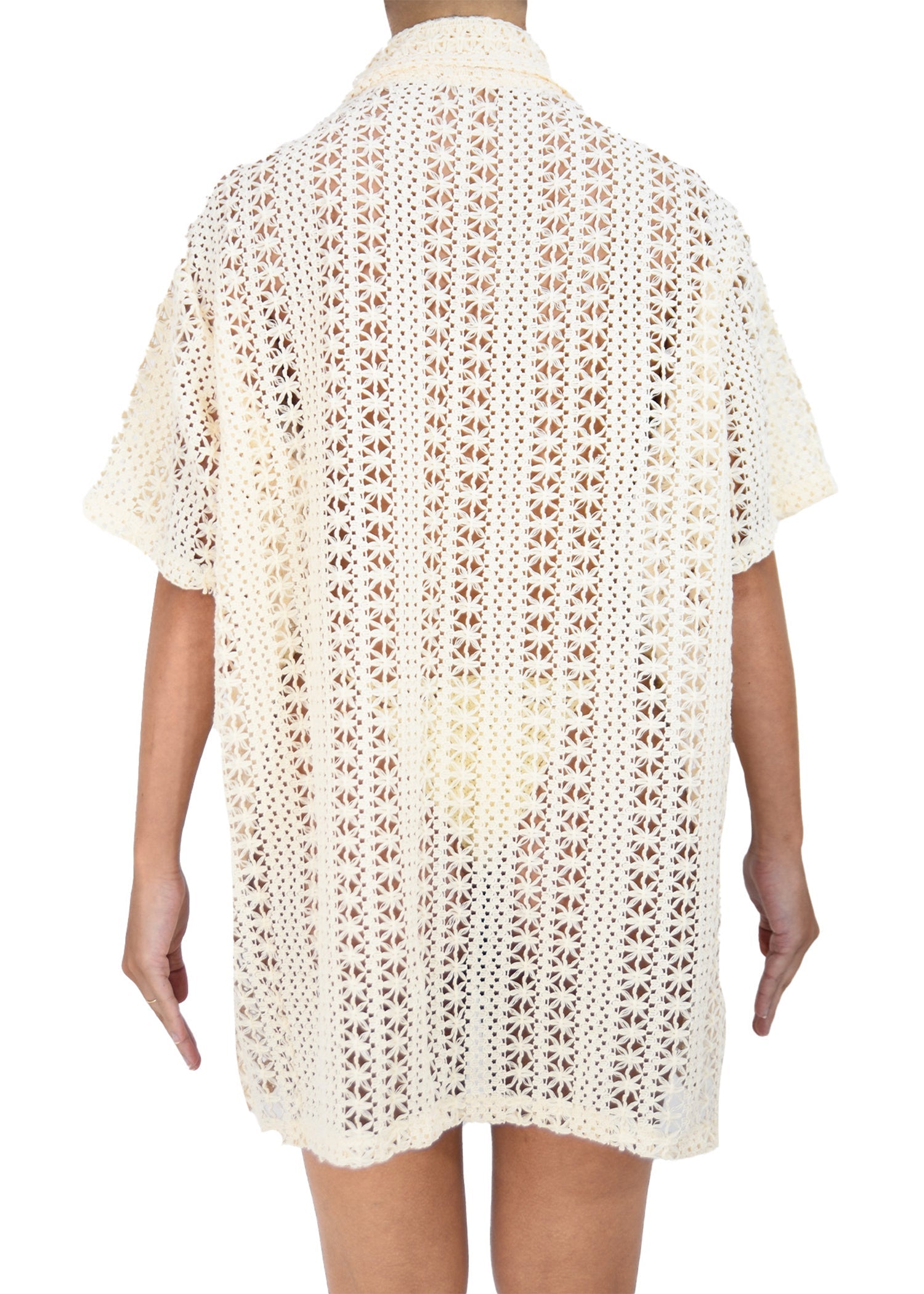 Back view of model wearing a beige, oversized, crocheted button-down featuring pearl button details.