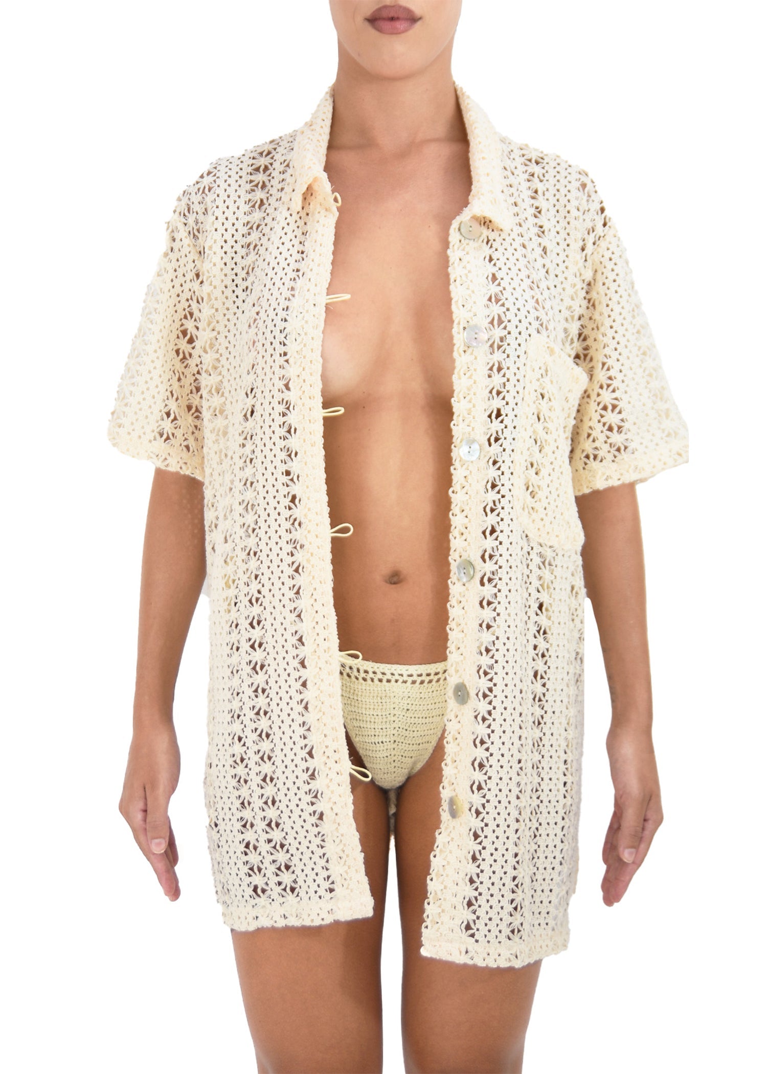 Model wearing a beige, oversized, crocheted button-down featuring pearl button details.